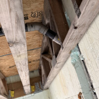 ReactNativeBlobUtilTmp e7l82malbc7zosf0s2t1cq Looking up through open floor joists showing black iron gas lines, PEX water lines, and PVC drain pipes strapped to framing.