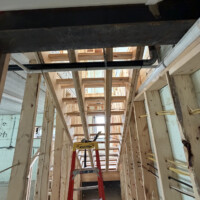 ReactNativeBlobUtilTmp hgv1rhqpn2cr54mzkoh20n Straight-on view of staircase framing showing overhead PVC drain, black iron gas line, and step ladder setup.