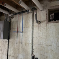 ReactNativeBlobUtilTmp majky0fge4nisy3qs3gtyp Open wall framing showing rerouted A/C condensate drain line running directly down to a basement floor drain.
