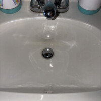 ReactNativeBlobUtilTmp o7m7bpjav1q741tu45ls79 White pedestal bathroom sink with popup stopper rod mechanism removed prior to drain body replacement.