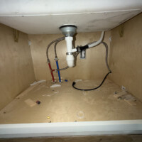 ReactNativeBlobUtilTmp rhffadxbte84knmqnkfxt Open kitchen sink cabinet base displaying drain tailpiece assembly, garbage disposal outlet, and PEX supply valves.