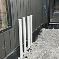 ReactNativeBlobUtilTmp y433jeqv10l4z1g3a9l953 Exterior wall of custom build showing four 3-inch PVC water heater vent pipes extending neatly through wall.