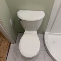 ReactNativeBlobUtilTmp d7rld1z4jl959tmmaqwzyf Newly installed white elongated toilet set on a light gray tile bathroom floor.