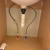 ReactNativeBlobUtilTmp lx8xbls0ikntqjmo016sxs Clean under-sink drain assembly featuring a PVC P-trap and flexible water supply lines inside a vanity.