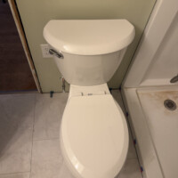 ReactNativeBlobUtilTmp tlvwgpt8p2wasv3eqw11c Installed white two-piece toilet positioned next to a fiberglass shower surround.